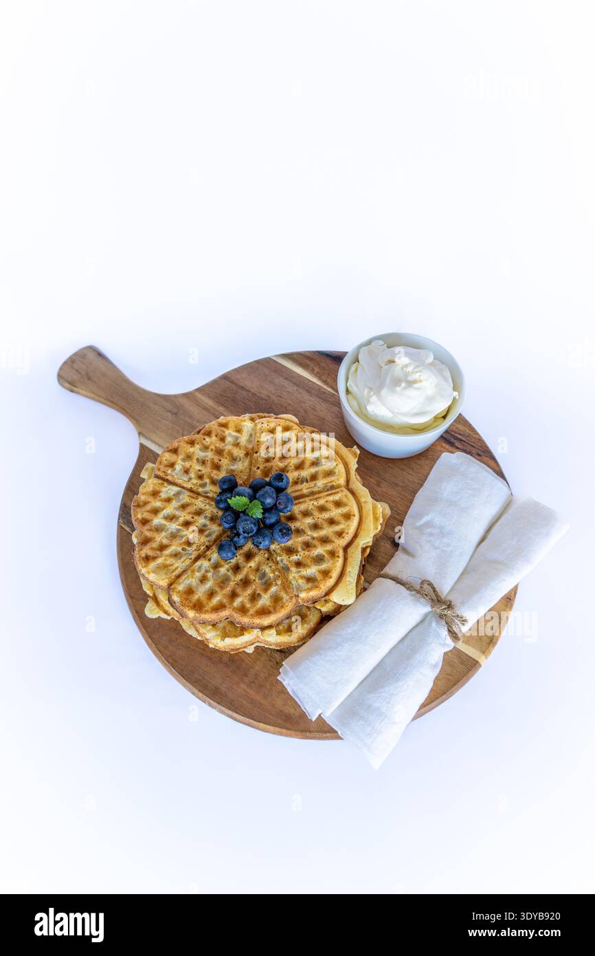Schwedische Waffeln in Herzform mit frischen Blaubeeren und Schlagsahne auf einem Holzbrett Stockfoto