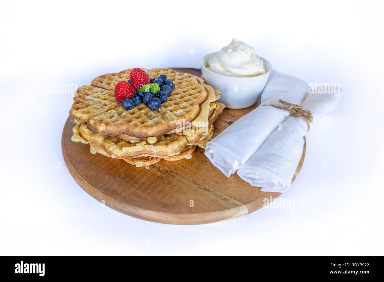 Schwedische Waffeln in Herzform mit frischen Heidelbeeren, Himbeeren und Schlagsahne auf einem Holzbrett Stockfoto