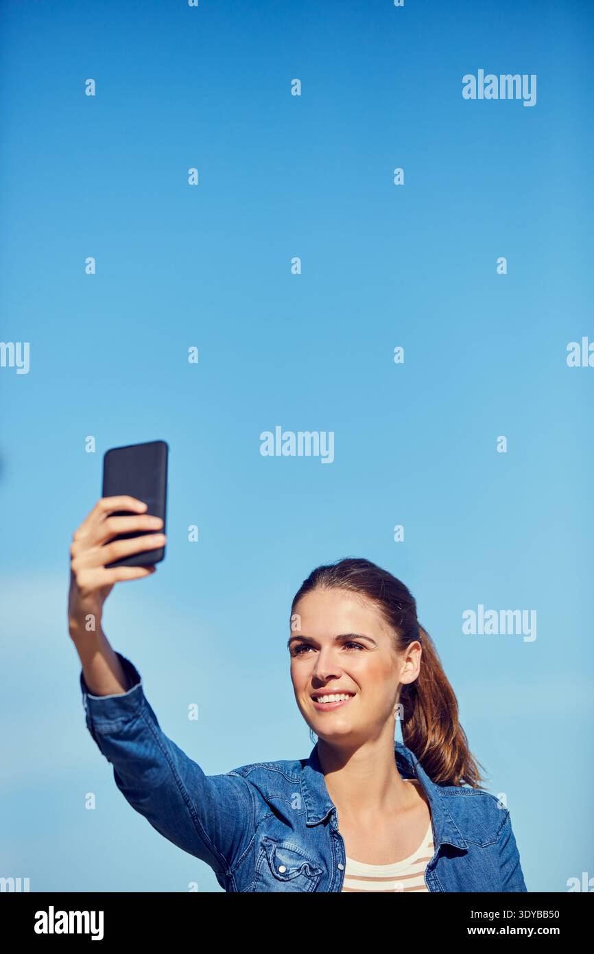 Glückliche Frau, blauer Himmel und entspannen Sie sich mit Selfie für Bilder, Fotos oder Momente im Weltraum. Weibliche Person, Benutzer oder Tourist mit Lächeln, App oder Stockfoto