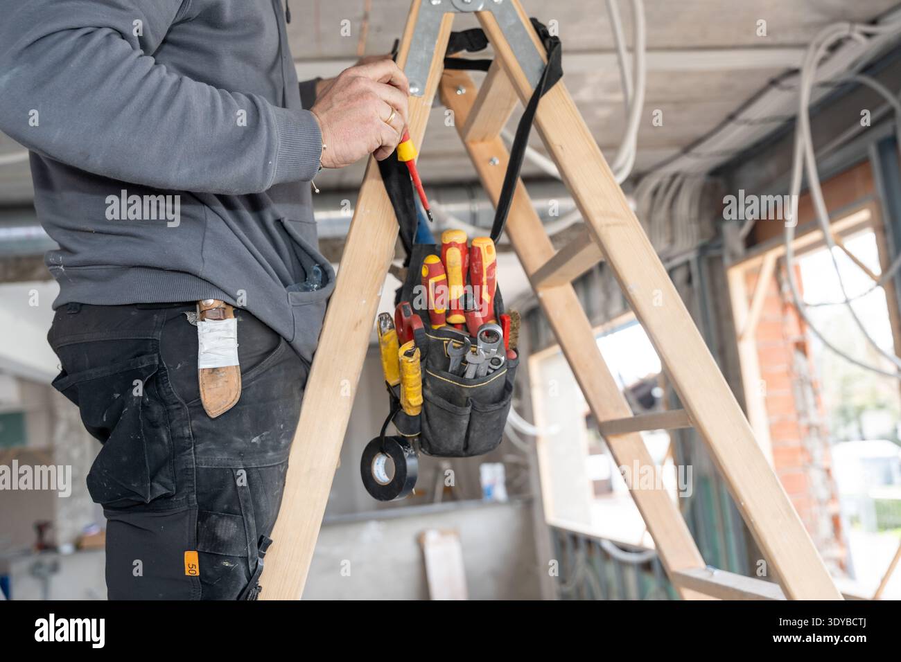 Bauarbeiter, der Kabel mit Werkzeugen an der Leiter montiert Stockfoto