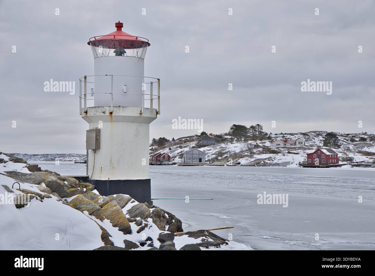 Kleiner weißer Leuchtturm mit rotem Dach an der gefrorenen Küste von Mollsund, Schweden. Nordisches Schifffahrtszeichen in einer Winterlandschaft mit Eis und Schnee Stockfoto