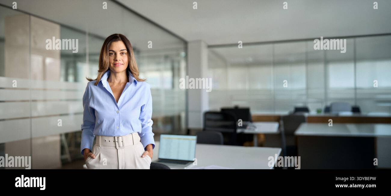 Geschäftsfrau mittleren Alters, die im Büro steht und in die Kamera blickt. Hochformat. Stockfoto