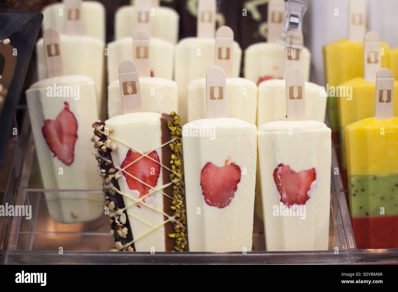 Reihen von weißen cremefarbenen Eis-Eis mit eingebetteten Erdbeerscheiben und Schokoladennussbelag in einer gekühlten Vitrine. Stockfoto
