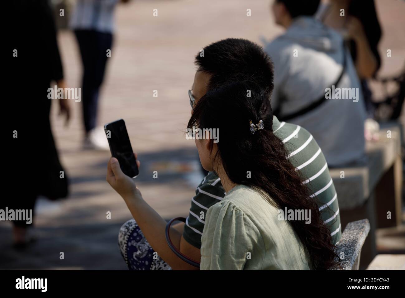 Touristen-Paar, das sich ausruht und Smartphone benutzt, zwangloses Telefonieren im Freien, entspannter digitaler Moment, privater Moment in der Öffentlichkeit, Seitenprofil Stockfoto