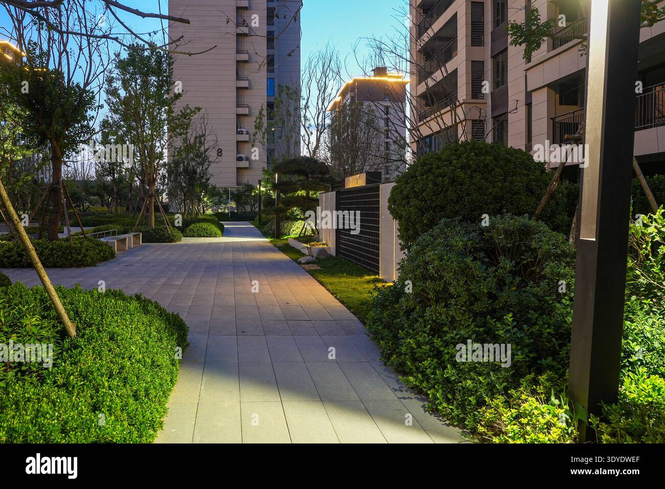 Ein strukturierter Gang führt durch einen lebendigen Wohngartenpark bei Sonnenuntergang. Das Bild vermittelt architektonische Ausgewogenheit, Gemeindeharmonie, Frieden Stockfoto