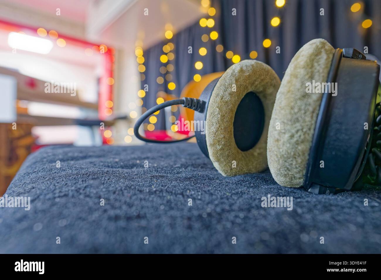 Ein Paar Vintage-Kopfhörer mit weichen Ohrkissen auf einer dunklen strukturierten Oberfläche mit warmen Bokeh-Lichtern im Hintergrund, die ein gemütliches atmos schaffen Stockfoto