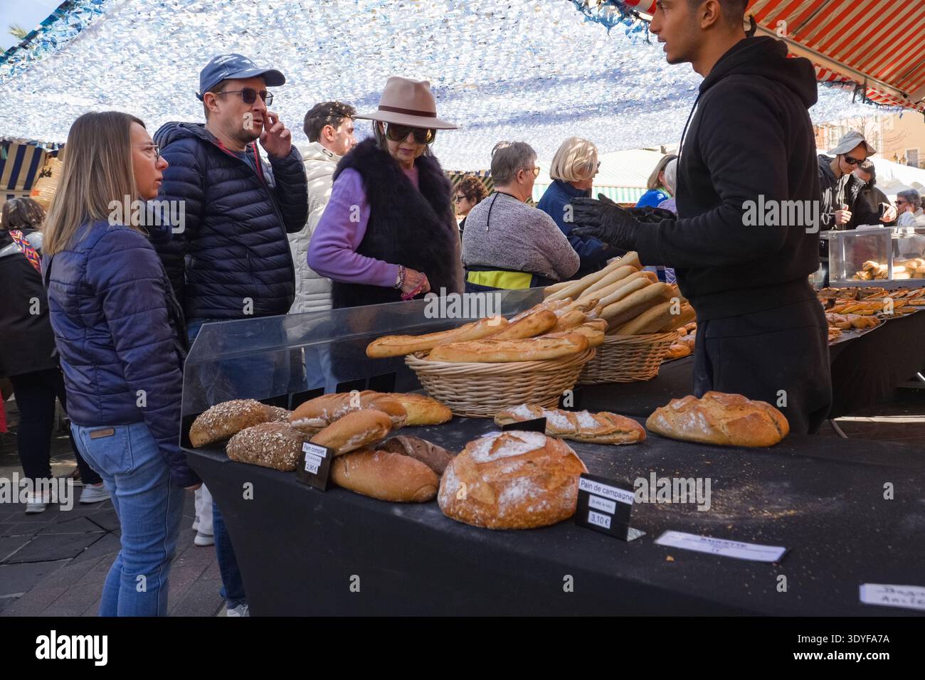 Auf dem Freiluftmarkt Cours Saleya in der Altstadt von Nizza, in der französischen Riviera-Szene, kaufen Käufer handwerkliches Brot. Stockfoto