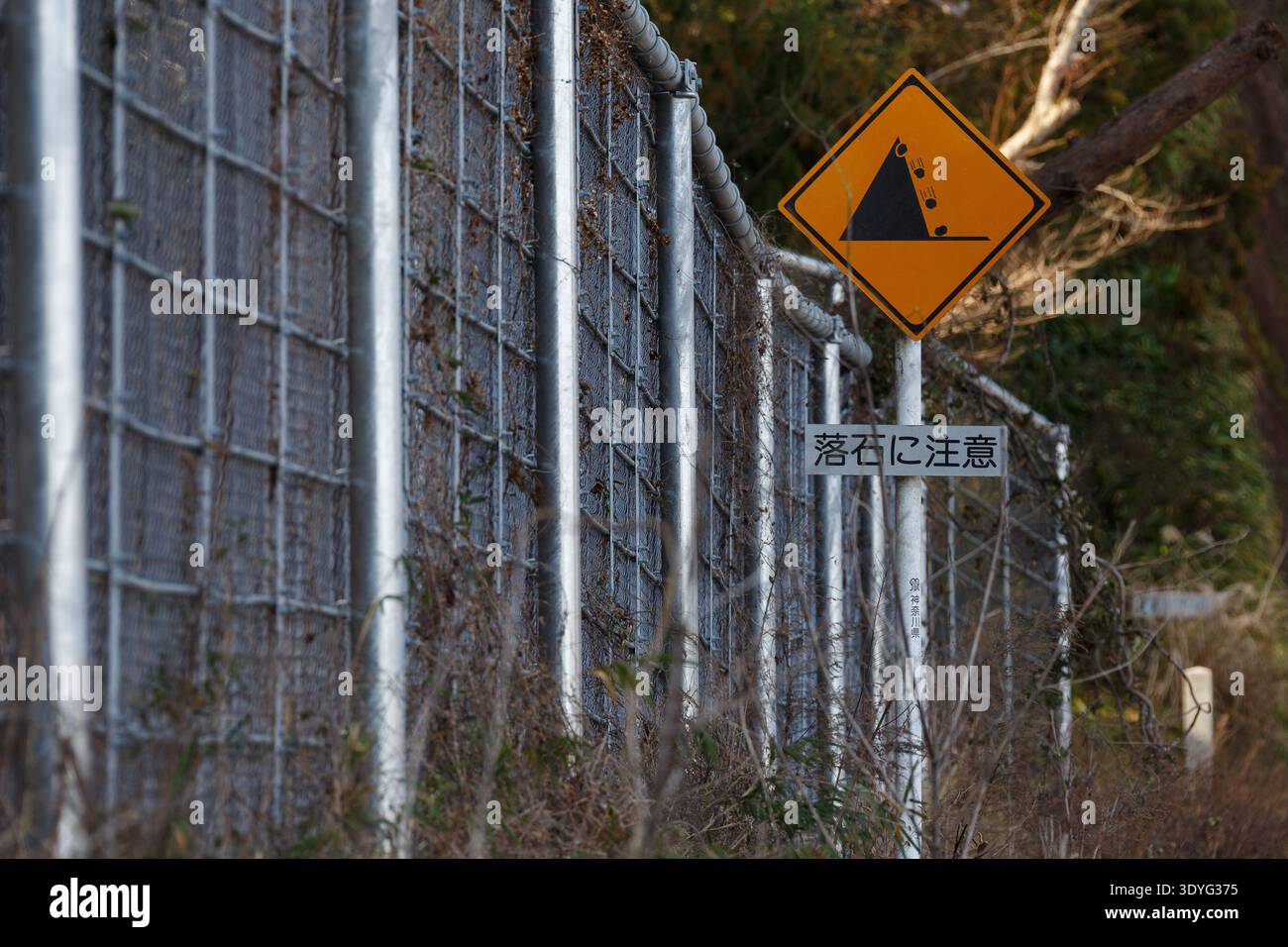 Ein großer Metallzaun zum Fangen herabfallender Felsen durch ein Schild, das vor herabfallenden Felsen warnt, am Straßenrand in der Nähe von Aikara im ländlichen Kanagawa, Japan. Stockfoto
