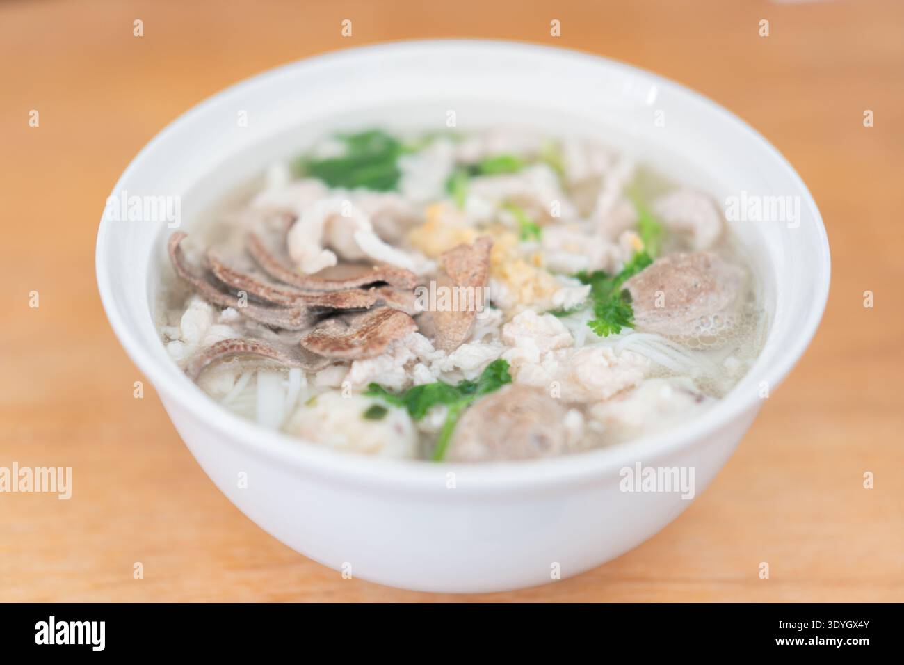 Vietnamesische Pho-Nudelsuppe mit Rinderkraut und Kräutern in der weißen Schüssel auf Holztisch Stockfoto