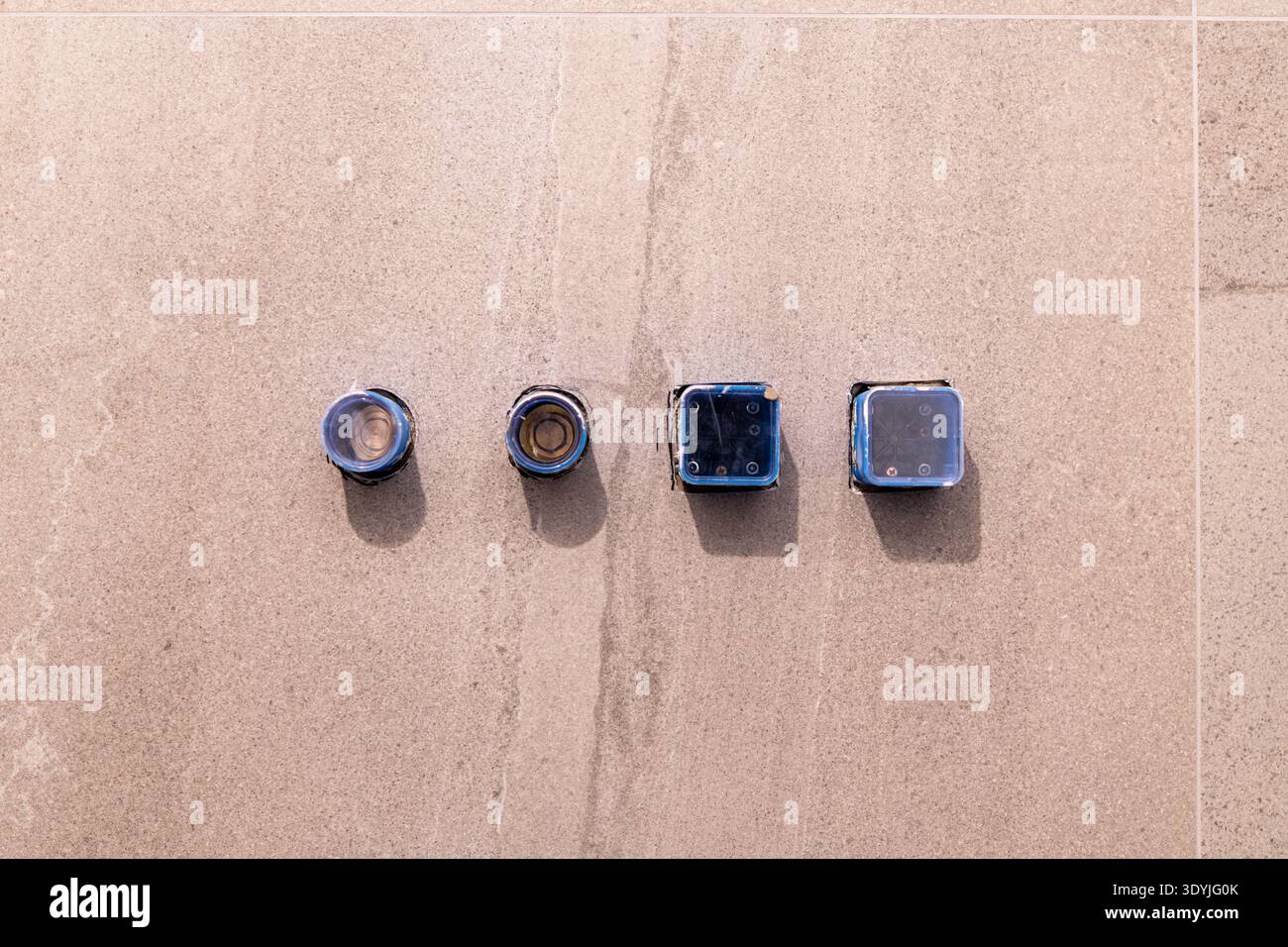 Vier vorstehende eingebaute Sanitärarmaturen auf beigen Badezimmerfliesen vor der Installation eines Wannenarmators sind in der Nähe sichtbar. Stockfoto