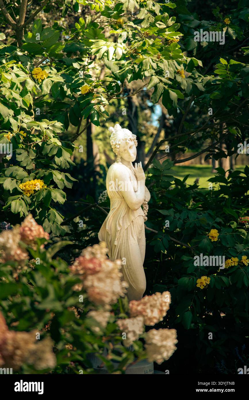 Eine klassische Marmorstatue zwischen grünem Laub und Blumen in Sydneys Royal Botanical Gardens, beleuchtet durch Sonnenlicht. Stockfoto