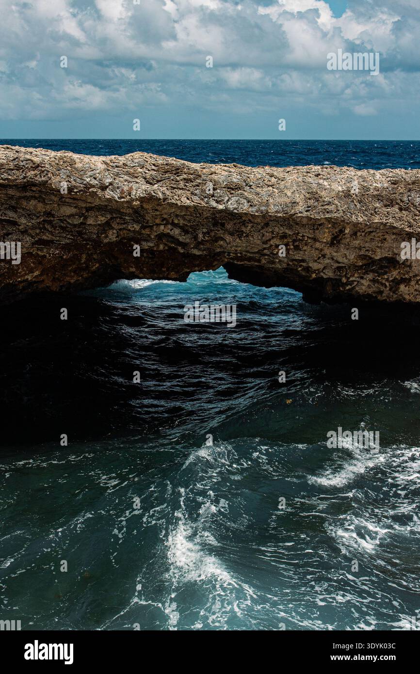 Eine alte natürliche Brücke über einem tiefblauen Ozean mit wildem Wasser und blauem Himmel. Stockfoto