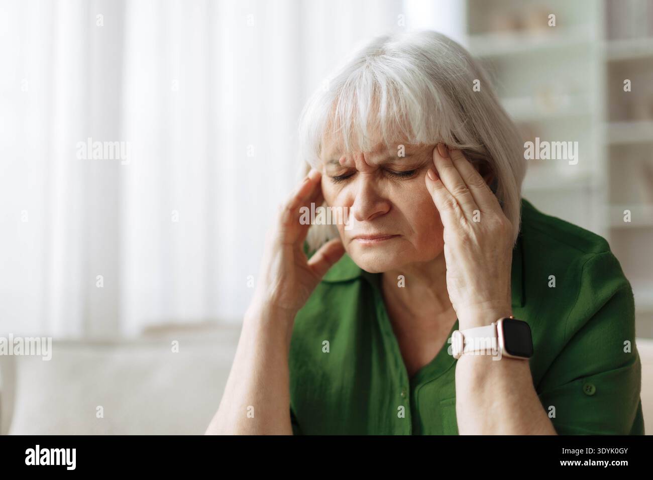 Ältere Frau berührt Schläfe, während sie zu Hause Kopfschmerzen hat Stockfoto