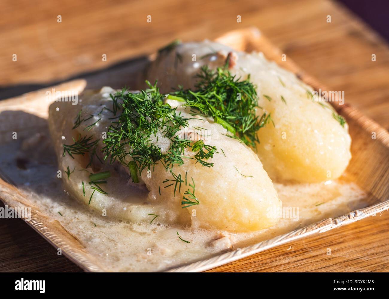 Cepelinai, traditionelle litauische Kartoffelknödel, serviert mit Sauerrahm und garniert mit knusprigen Speckstückchen und frischer Petersilie Stockfoto