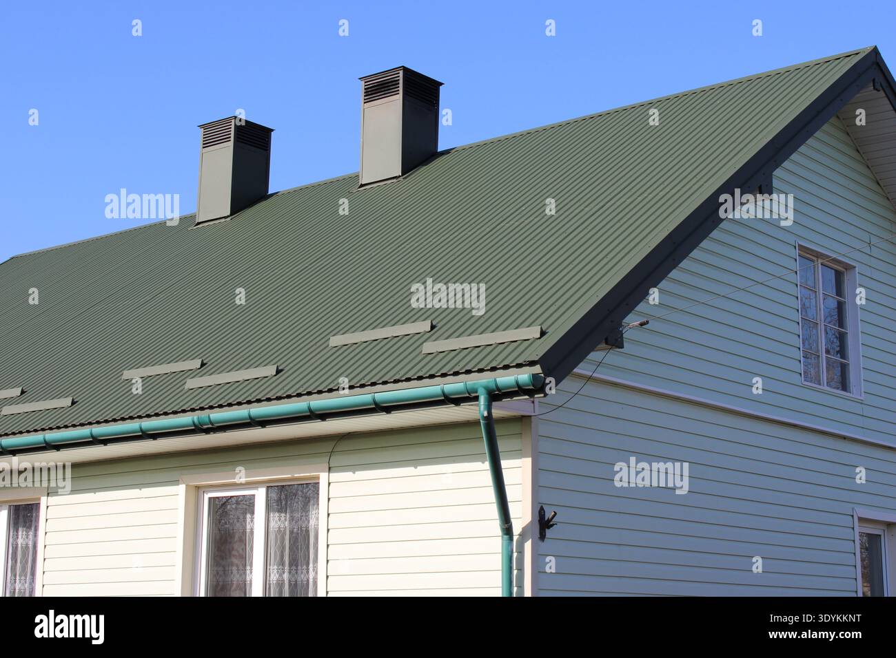 Dieses Haus verfügt über ein begrüntes Dach und zwei Kamine. Die Wände sind hell gestrichen und der Himmel ist klar. Es zeigt die Struktur in einem ruhigen Viertel Stockfoto