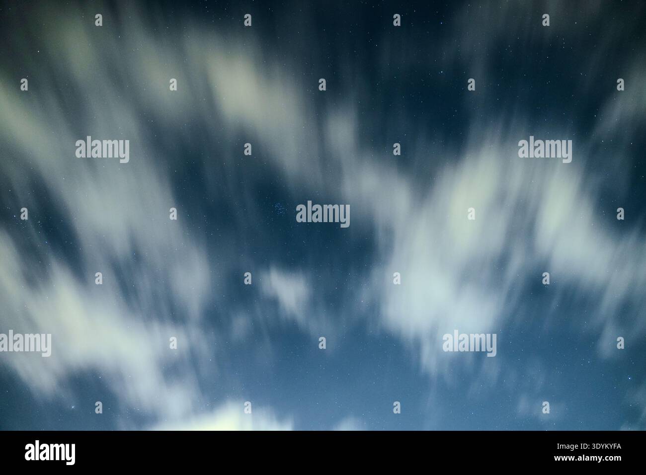 Langzeitbelichtung Aufnahme von Nachtwolken, die langsam über einen tiefblauen Himmel fließen und verstreute Sterne zwischen den weichen weißen Wolkenstreifen und den Kreationen freigeben Stockfoto