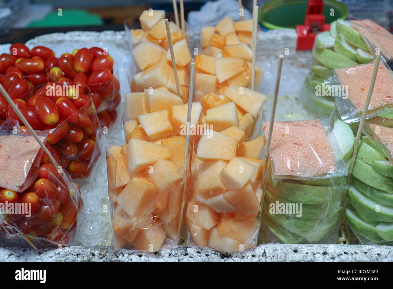 Frisch geschnittenes Obst in Plastiktüten mit Chili-Salz-Dip auf dem thailändischen Straßenmarkt, der farbenfrohe gesunde Snacks und authentische lokale Esskultur zeigt. Stockfoto