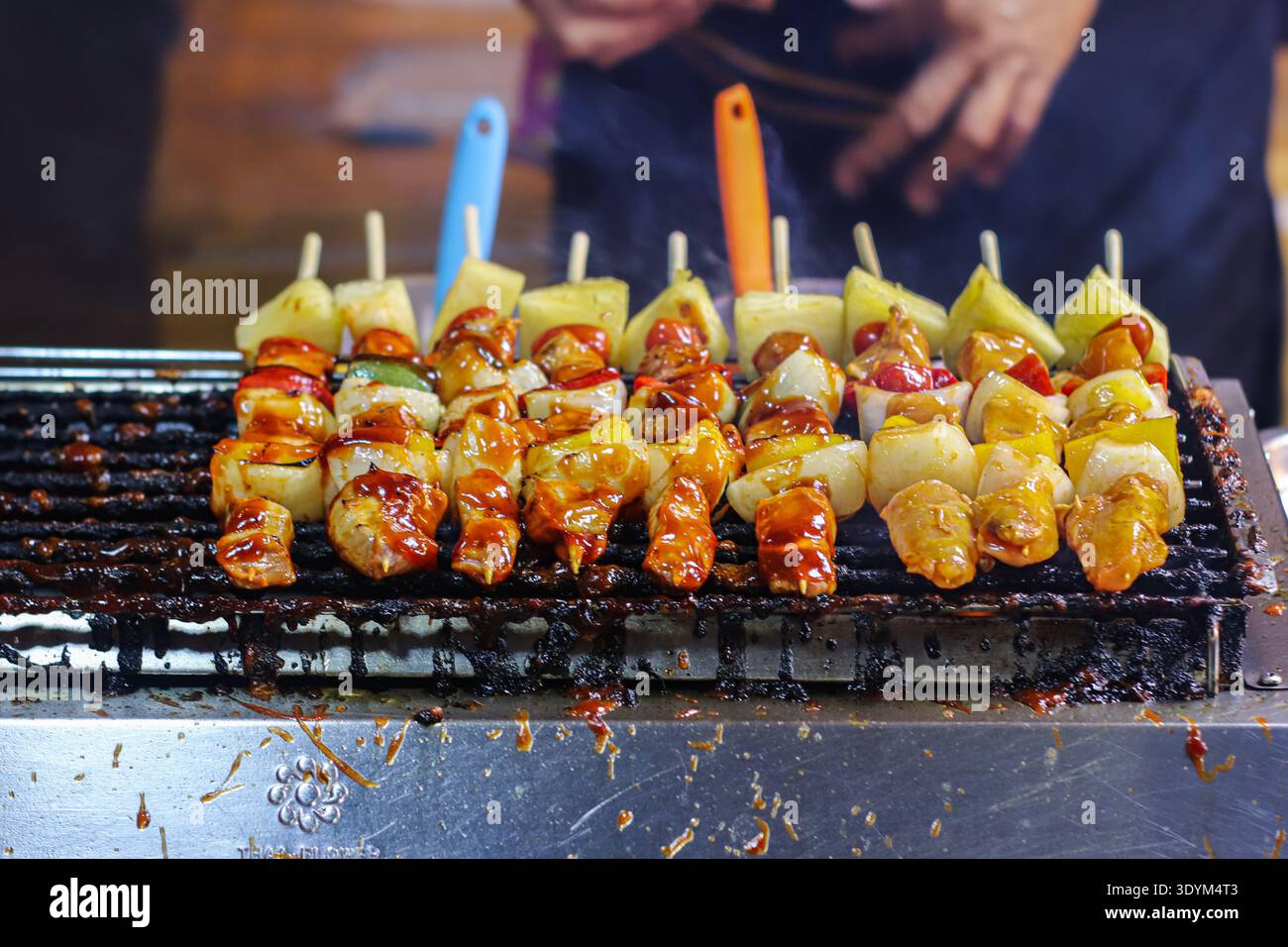 Thailändische Grillspieße mit Hähnchen Ananaszwiebeln und Paprika, die über Holzkohle gegrillt werden, an einem belebten Nachtmarkt Street Cuisine Stand. Stockfoto