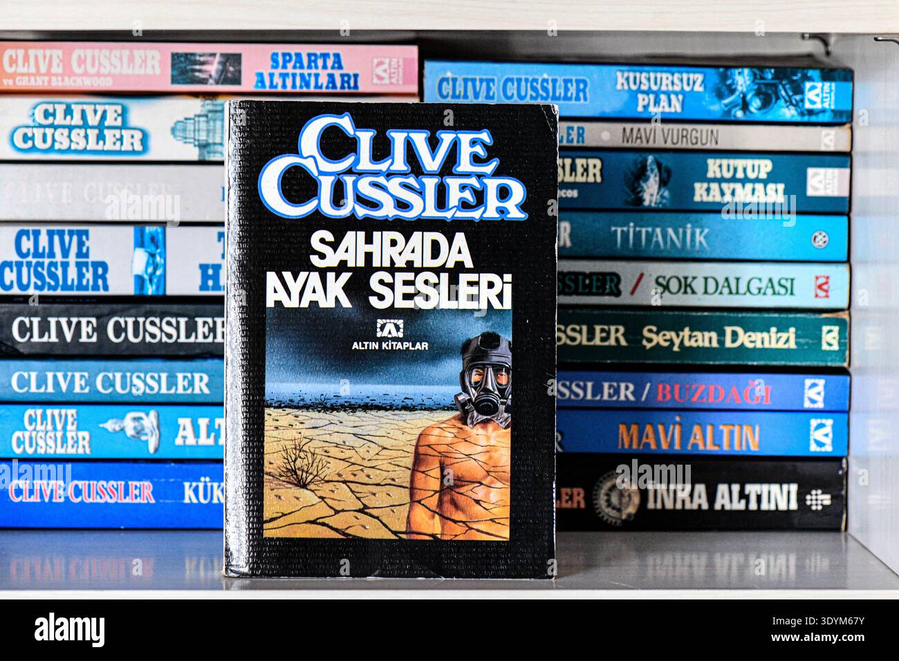 Eine türkische Ausgabe von Clive Cusslers Roman Sahrada Ayak Sesleri Originalname Sahara, stehend vor einem Regal mit anderen übersetzten Abenteuerbüchern. Stockfoto