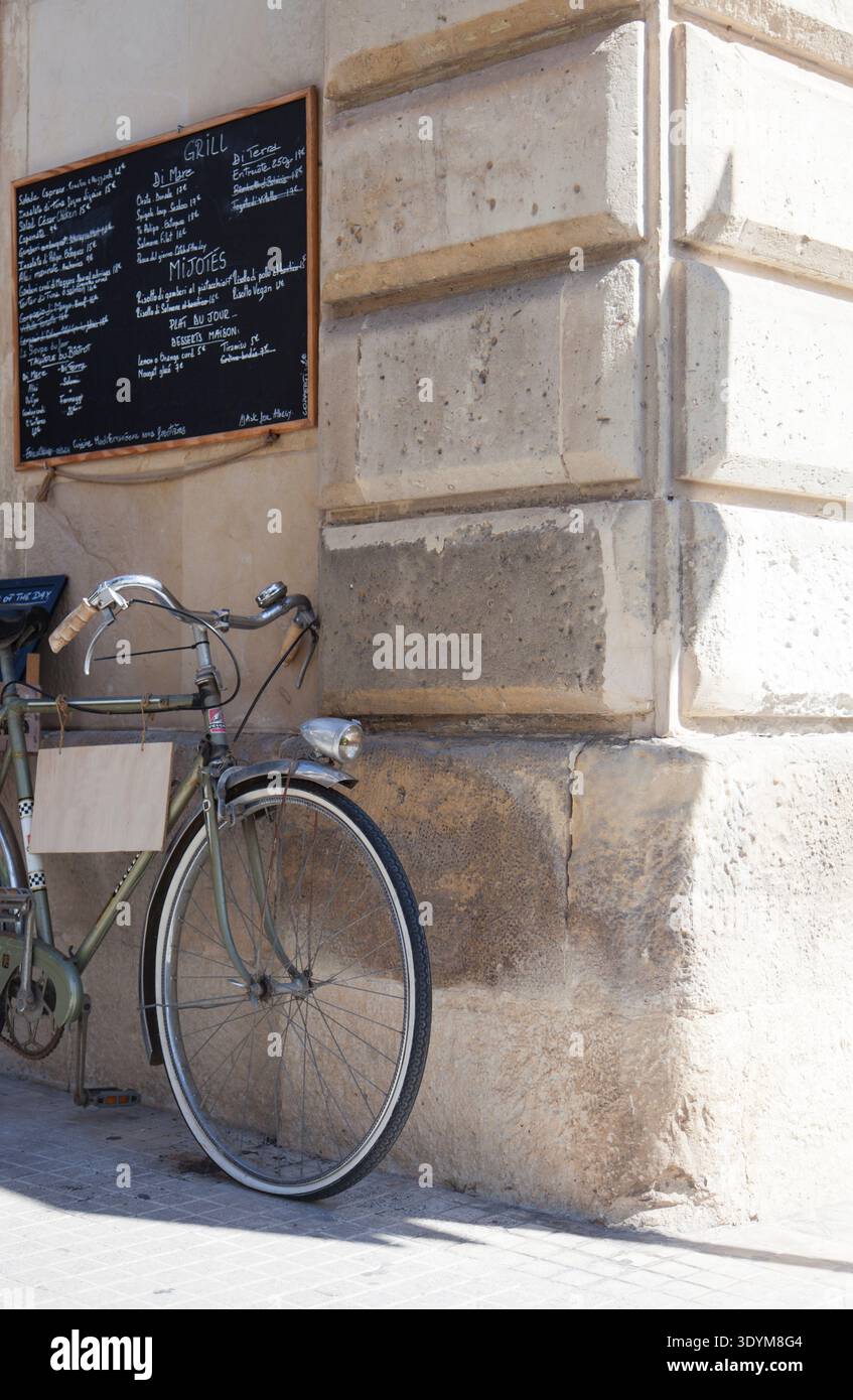 Ein altes Fahrrad, das an eine Wand gelehnt ist, mit einem Menü darüber, vor einem Restaurant Stockfoto