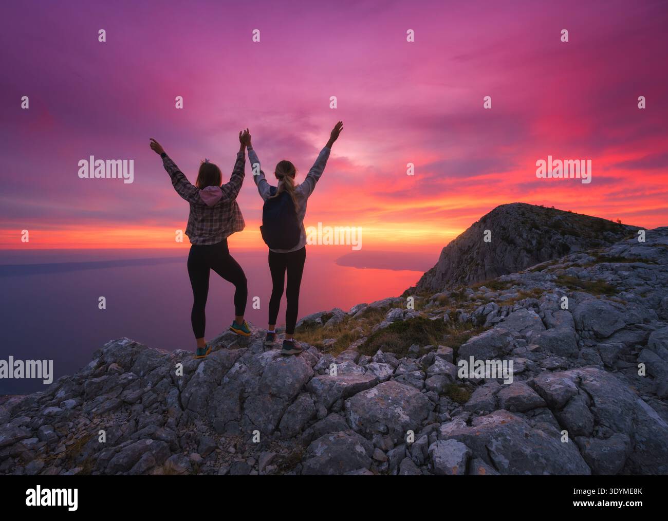 Zwei Frauen mit Rucksäcken und Arme auf den Bergen bei Sonnenuntergang Stockfoto