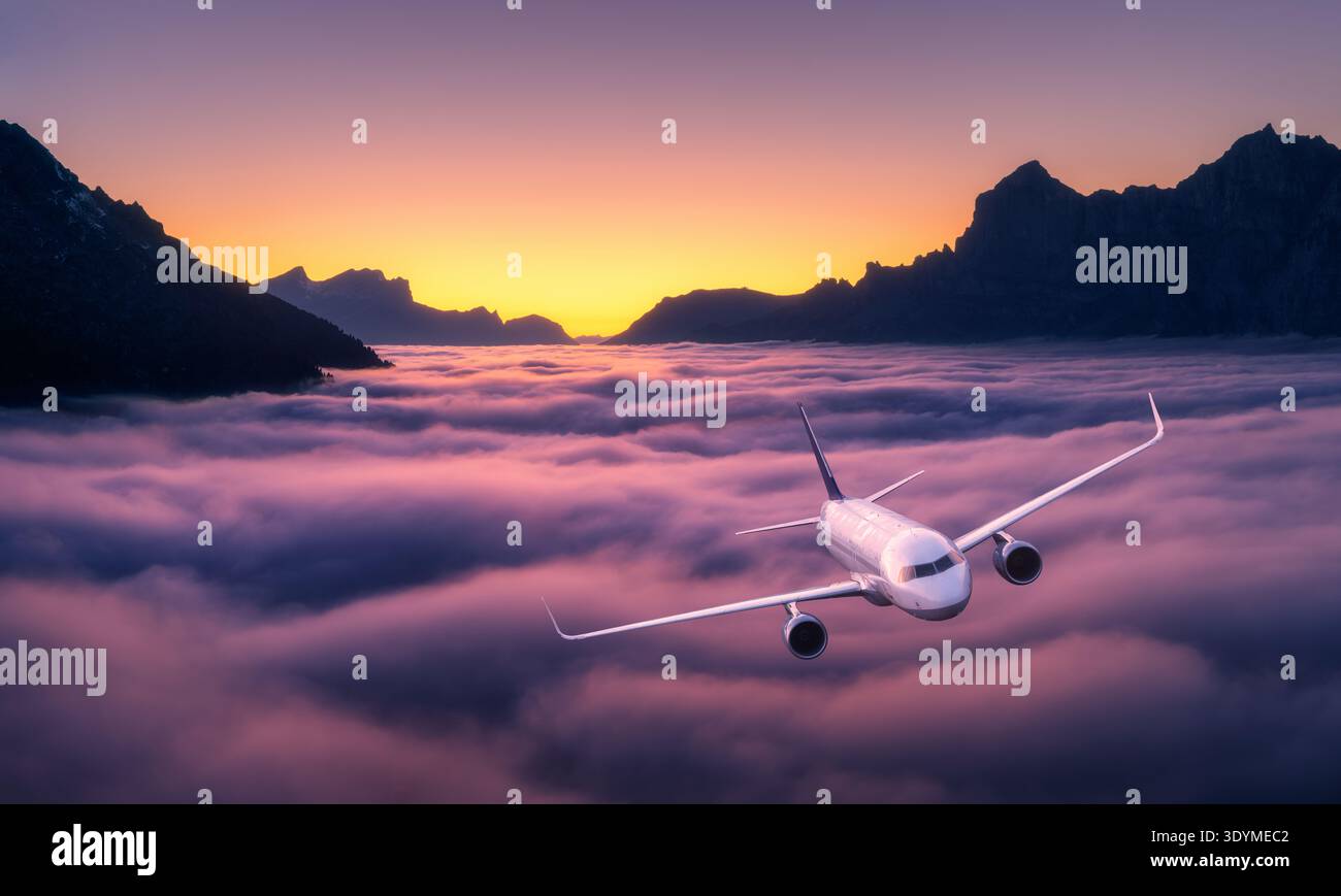 Kommerzielles Flugzeug fliegt über violetten und rosa Wolken, Berg Stockfoto