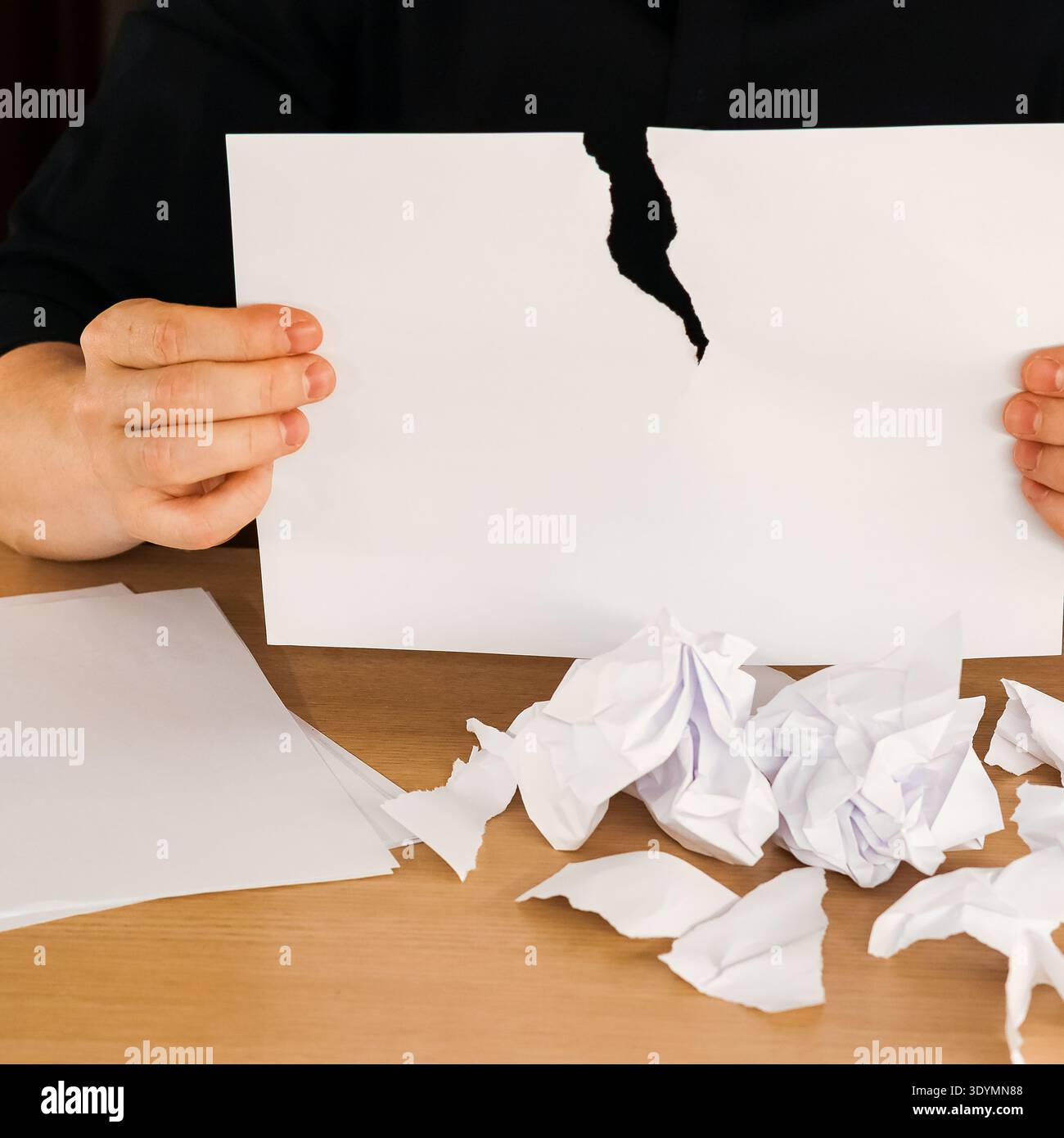 Hände heben ein gerissenes Blatt mit schwarzer Tränenspur über dem Holztisch mit verstreuten Schrott Stockfoto