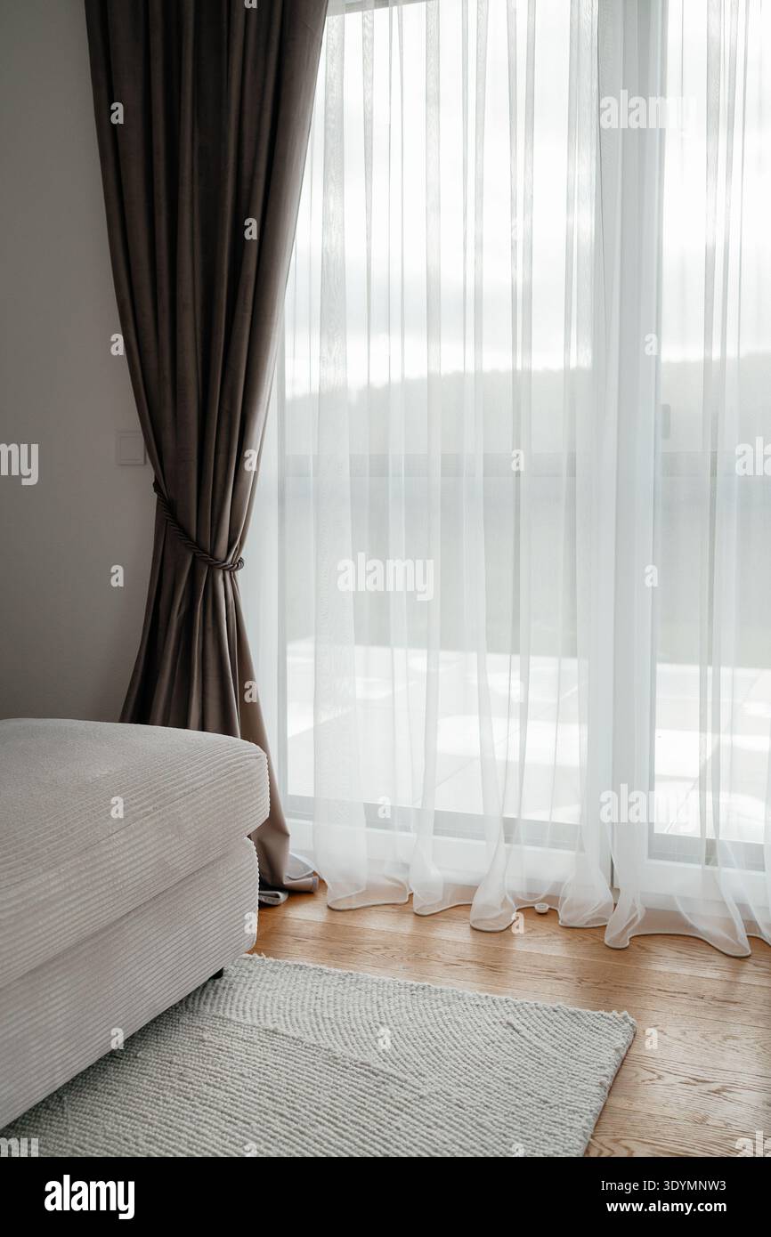 Helles Wohnzimmer mit großem Fenster, transparenten Vorhängen und Tageslicht. Gemütliches, modernes Ambiente mit sanftem Licht, das in den Raum eindringt Stockfoto