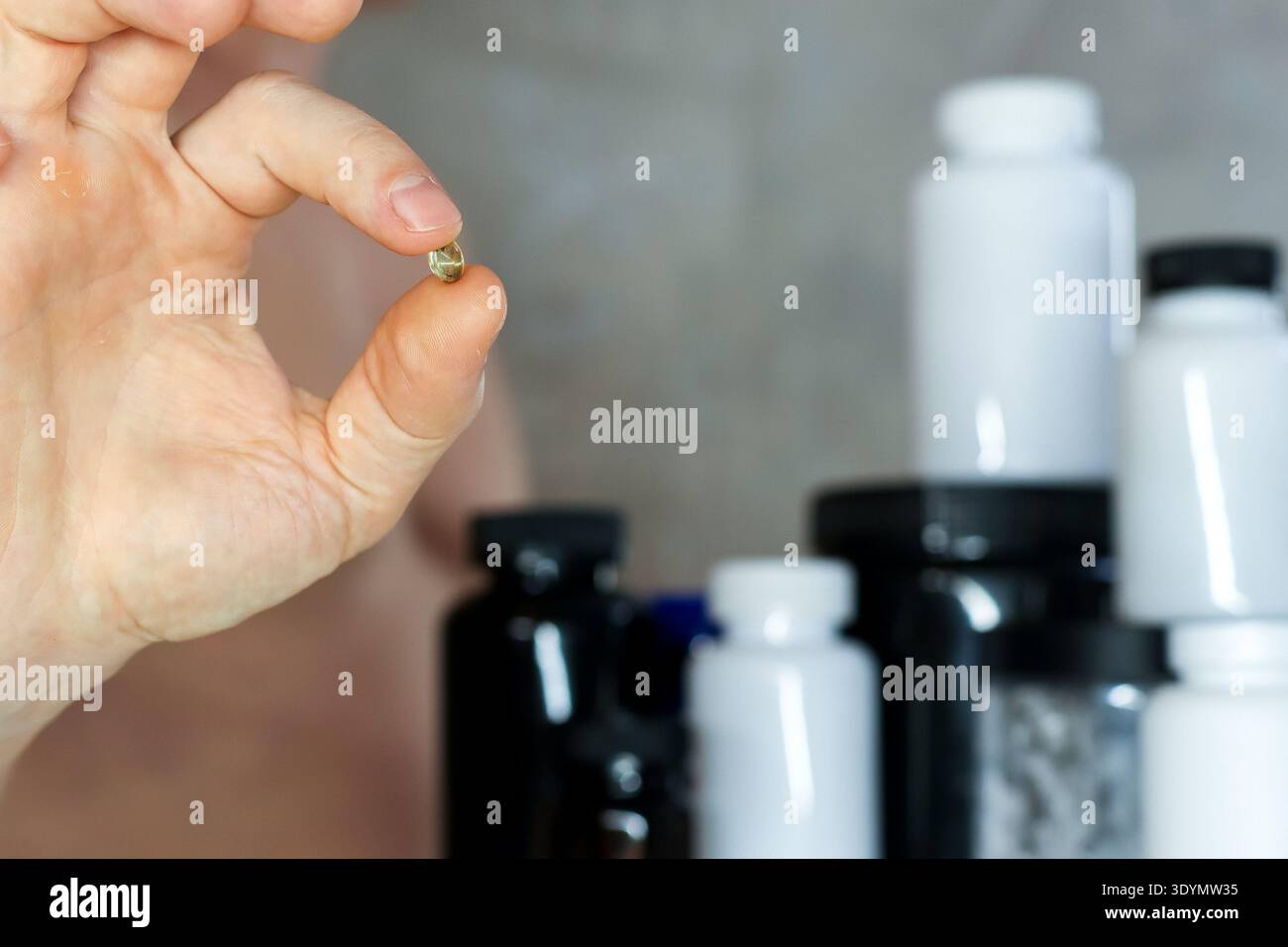 Mann, der kleine Kapseln gegen Supplementgefäße präsentiert. Sportlicher Mann, der eine Nahrungspapsel mit einer Reihe von Nahrungsergänzungsbehältern hochhält i Stockfoto