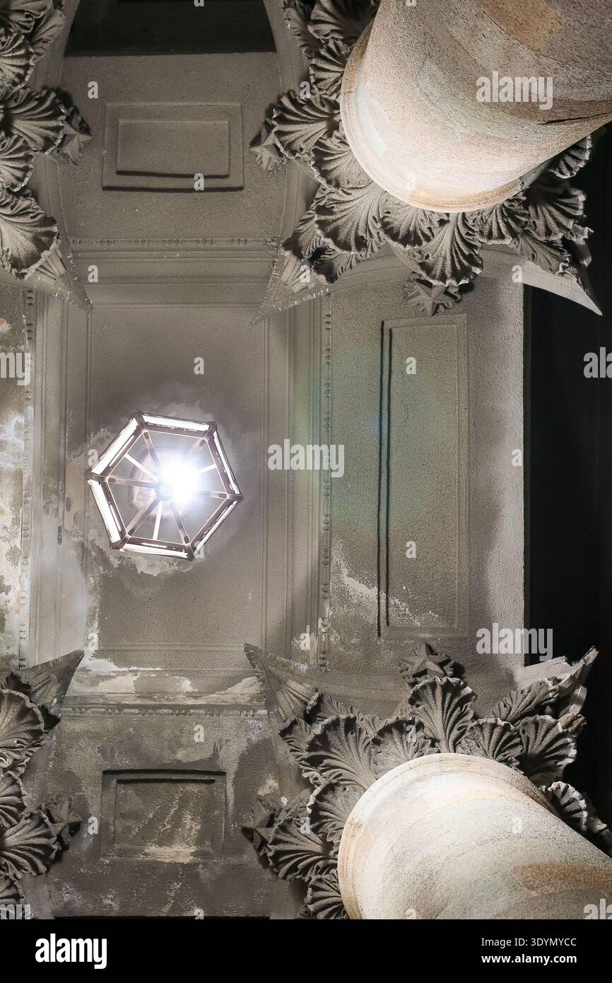 Nahaufnahme niedriger Winkel der hellen hängenden Laterne, die Licht auf reich verzierte Gipsdecke und Säulenkapitelle im alten historischen Innenraum wirft Stockfoto
