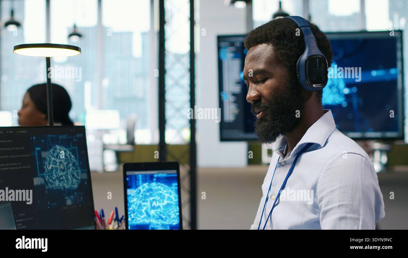 Computerwissenschaftler im Büro, der KI-Systeme für maschinelles Lernen integriert, um Workflows zu optimieren und Kopfhörer zu erhalten. afroamerikaner benutzt künstliche Intelligenz auf Geräten, Musik hören, Kamera A Stockfoto