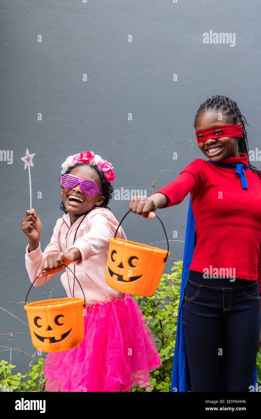 Afroamerikanische Kinder posieren an der grauen Wand mit Tutu und cape mit Kürbiseimern Stockfoto