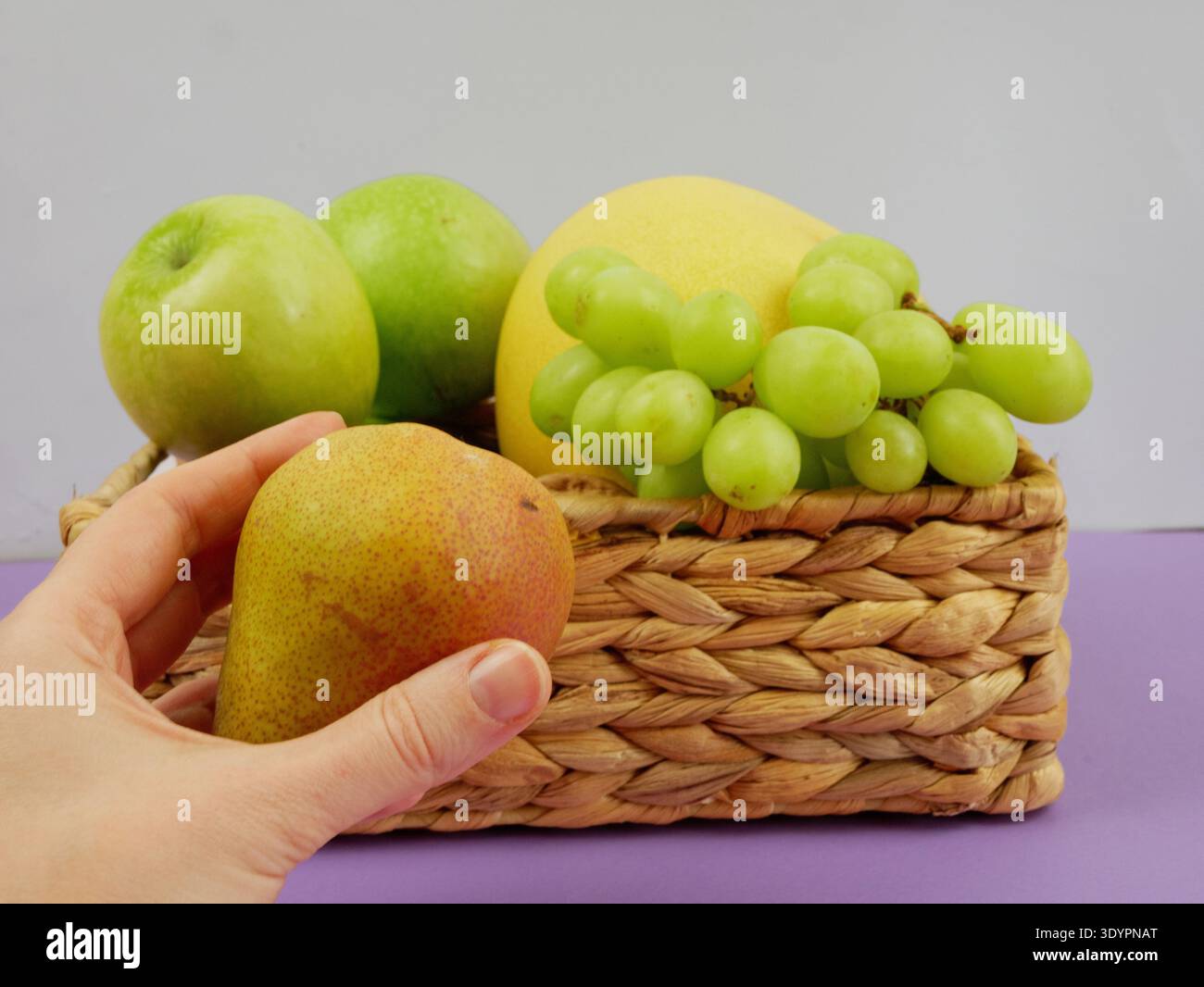 Gesunde Ernährung Lebensstil Konzept: Weibliche Hand wählt eine reife Birne aus einem Korb mit Trauben, Äpfeln und Melone Stockfoto