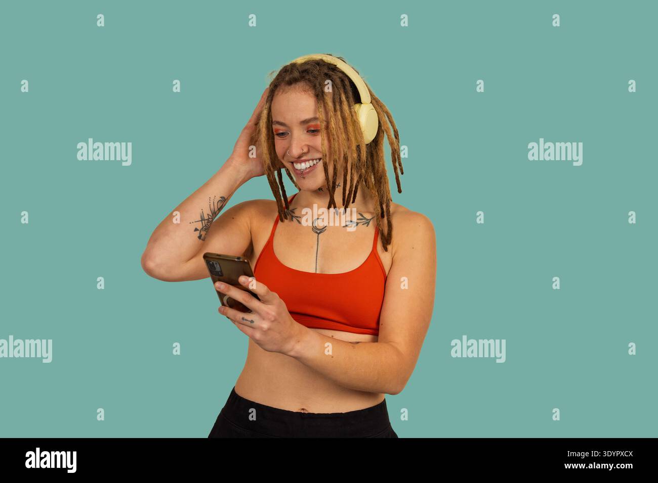 Junge Frau mit Dreadlocks lächelt, hört Musik über Kopfhörer und hält ein Smartphone Stockfoto