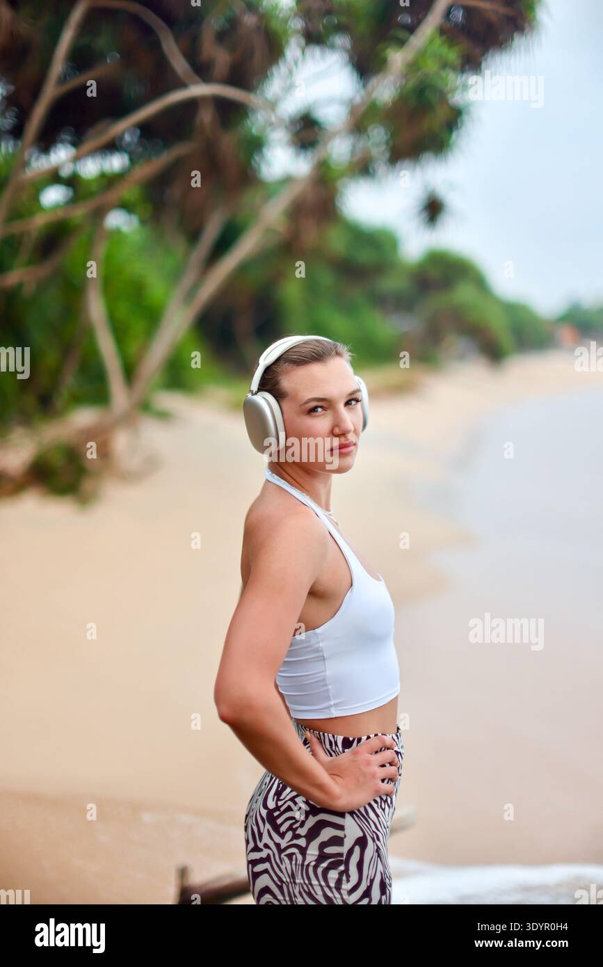 Selbstbewusster Strandsportler. Energiegeladene Athletin, Die Den Küstenstil Mit Musikgenuss Genießen Kann Stockfoto