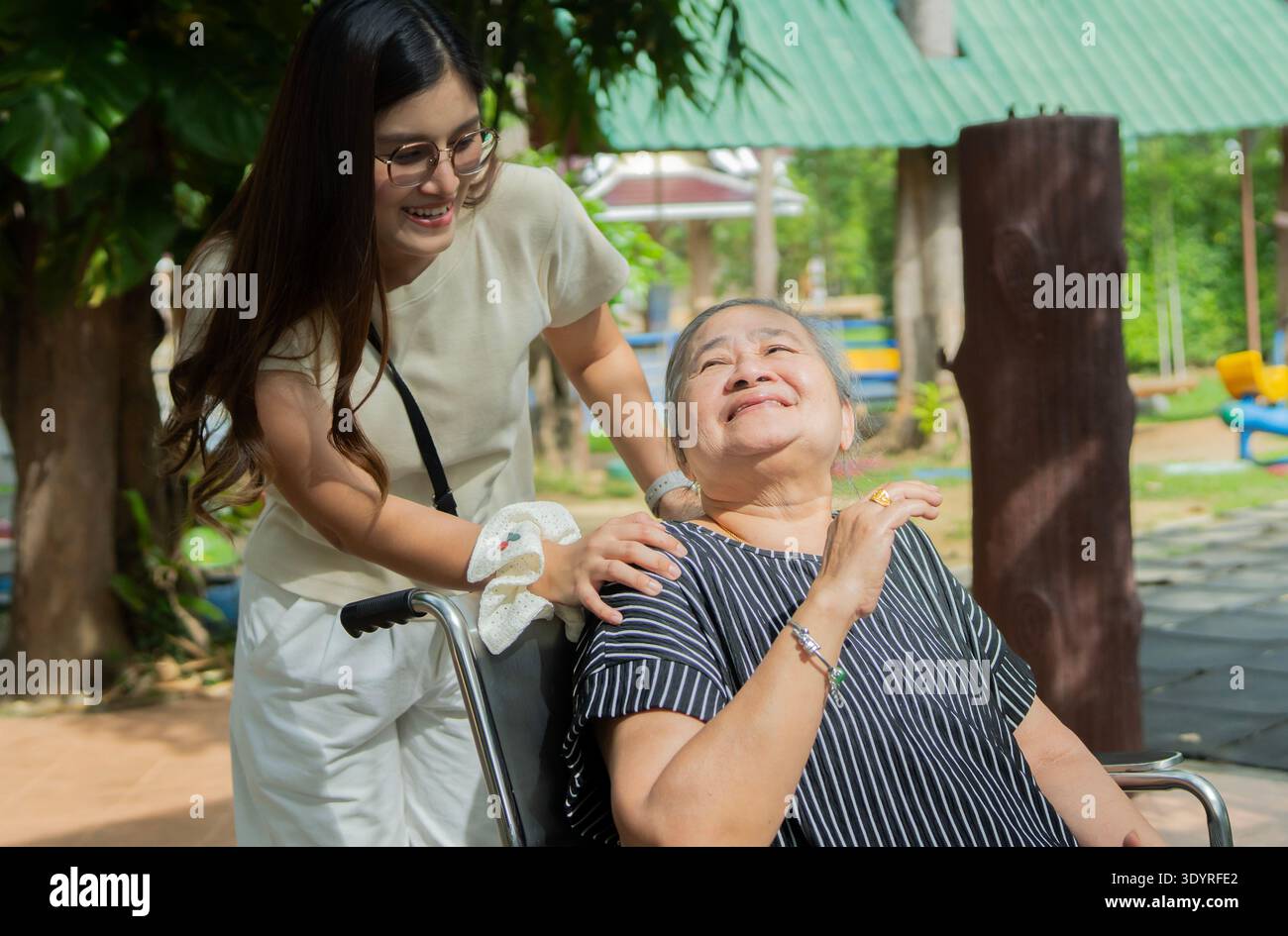 Glückliche asiatische Seniorengroßmutter und Kindermädchen, die sich im Park entspannen. Lächelnde ältere Frau im Rollstuhl mit Enkelin, die Spaß hat und mich redet Stockfoto