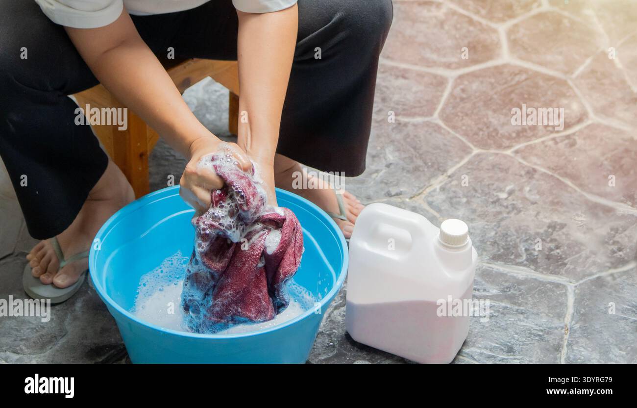 Hochwinkelansicht der weiblichen Handwäsche im blauen Becken mit der Waschmittelflasche. Wäschekonzept Stockfoto