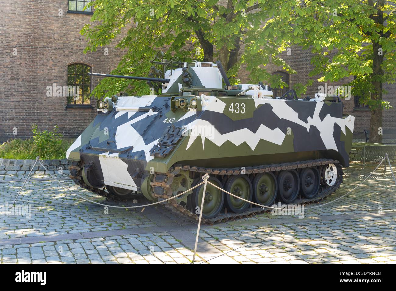 Der Blick auf einen Militärpanzer mit Tarnmuster befindet sich deutlich auf einer Kopfsteinoberfläche in der Nähe eines alten Backsteingebäudes in Oslo, Oslo, Norwegen. Stockfoto