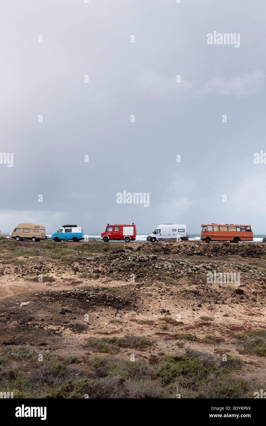 Eine Reihe farbenfroher Wohnmobile parkt entlang der zerklüfteten Atlantikküste in der Nähe von El Cotillo auf den Kanarischen Inseln Fuerteventura mit vulkanischem Gelände und dramatischem Schauspiel Stockfoto