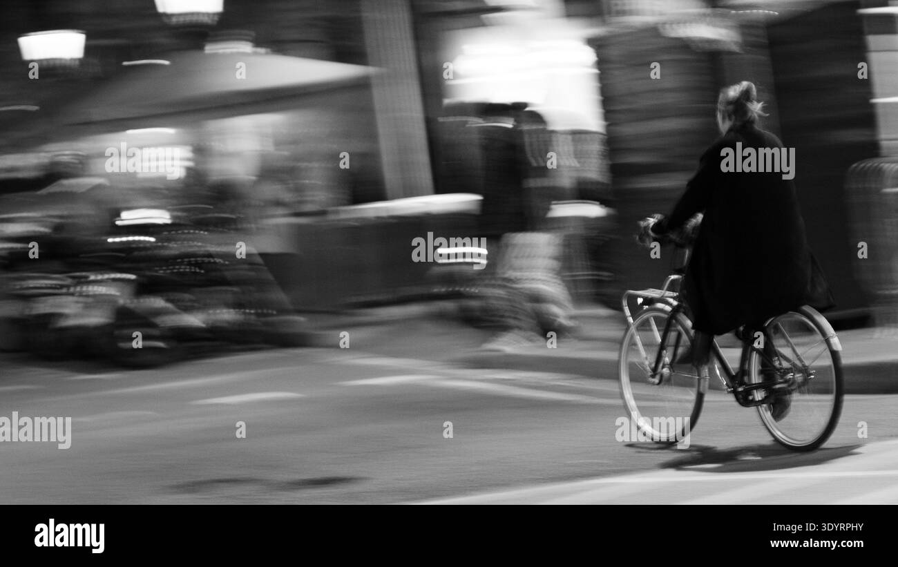 Frau, die auf einer europäischen Stadtstraße Fahrrad fährt, Bewegungsunschärfe-Effekt, schwarz-weiß. Stockfoto