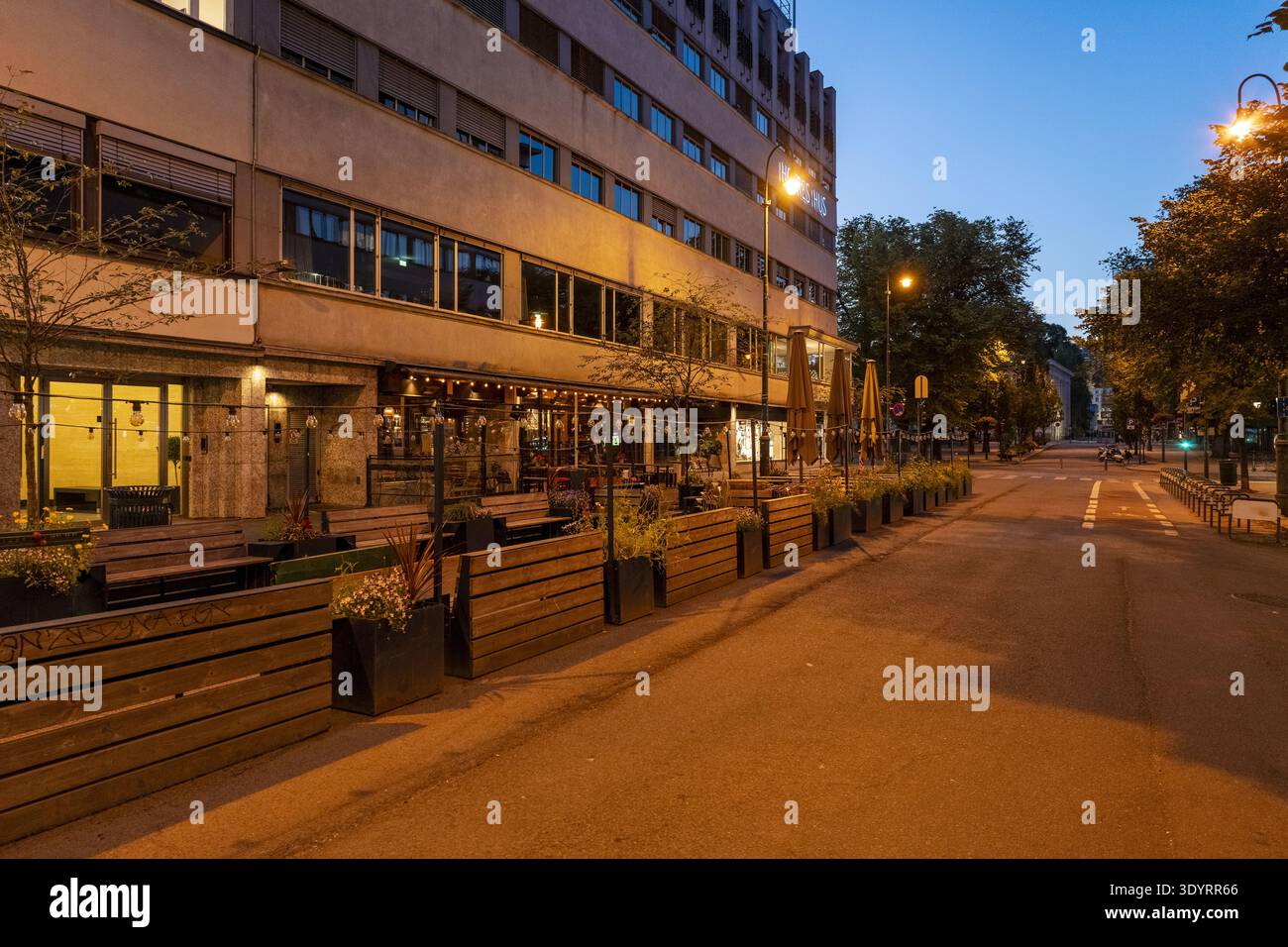 Blick auf das warme Leuchten der Straßenlaternen reflektieren von der leeren Straße, erhellen die moderne Architektur und einladende Sitzplätze im Freien, Oslo, Nor Stockfoto