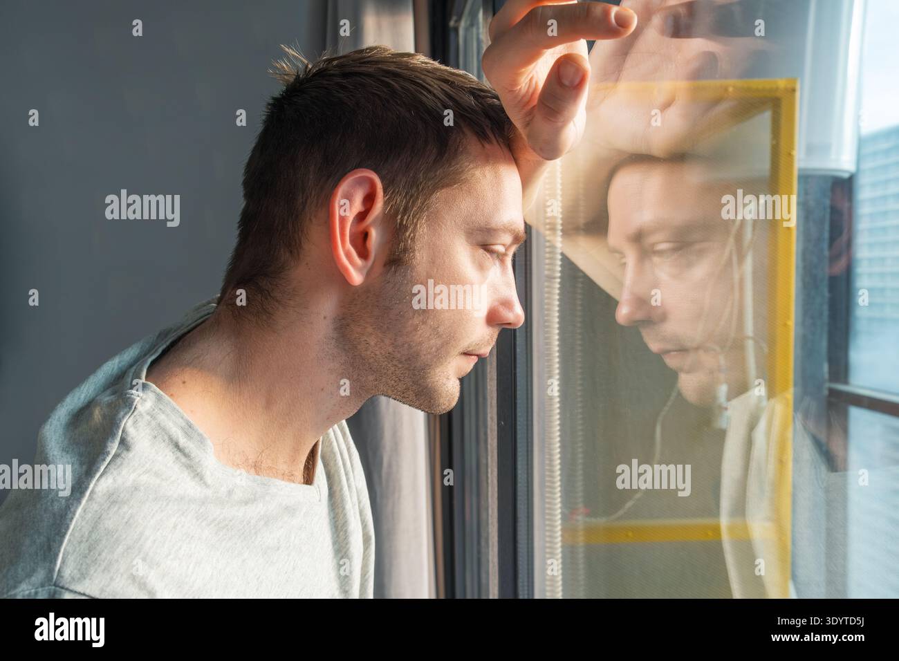Trauriger Mann, der durch das Fenster blickt, mit Reflexion, Einsamkeit und Depression zu Hause. Nachdenklicher Mann in ruhigem Moment der Traurigkeit und des selbst Stockfoto