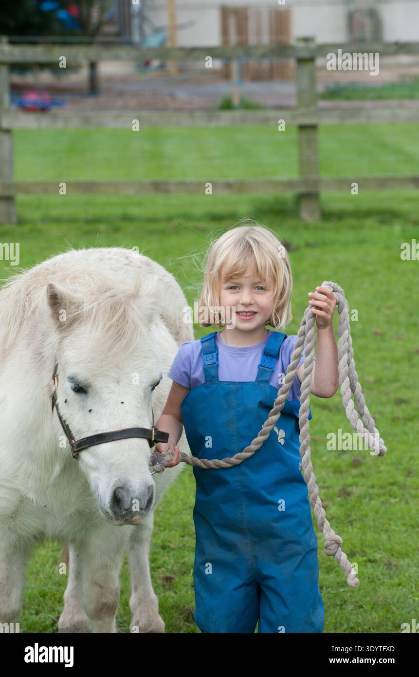 Kinder im Grundschulalter genießen einen lehrreichen Tag in der britischen Landschaft und interagieren eng mit traditionellen landwirtschaftlichen Nutztieren. Die Gruppe wird beobachtet, wie sie Hühner auf einem Bauernhof vorsichtig füttert, die sanfte Natur von weidenden Schafen beobachtet und mehr über Pferdepflege lernt, während sie Pferde und Ponys trifft. Diese überwachten Interaktionen bieten wichtige Lernerfahrungen im Freien und vermitteln Schülern in einer sicheren, praxisnahen Umgebung mehr über das Wohlergehen von Tieren, das ländliche Leben und die Herkunft ihrer Nahrung. Stockfoto