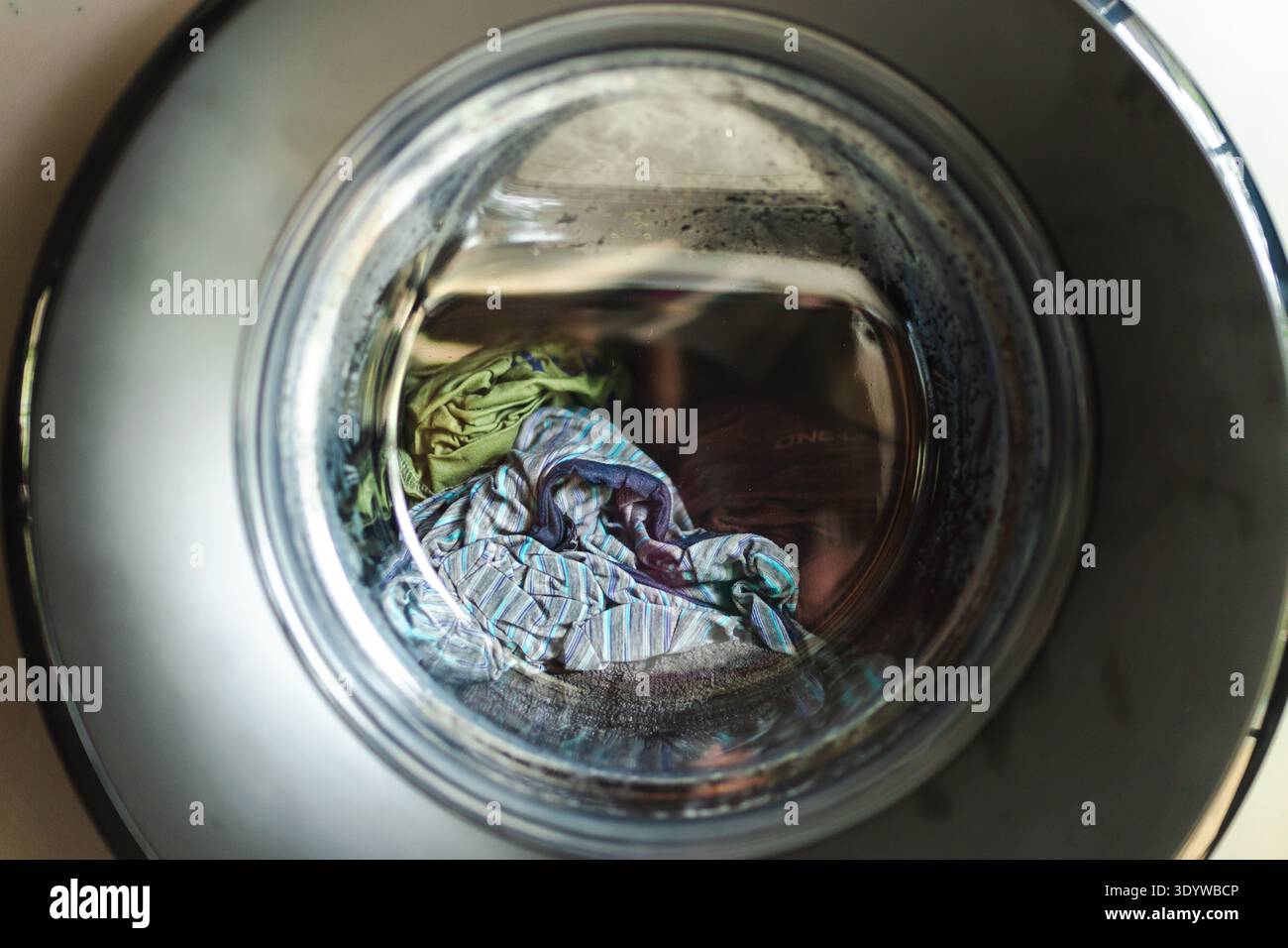 Wäschekleidung in der Waschmaschinentrommel durch eine runde Glastür Stockfoto