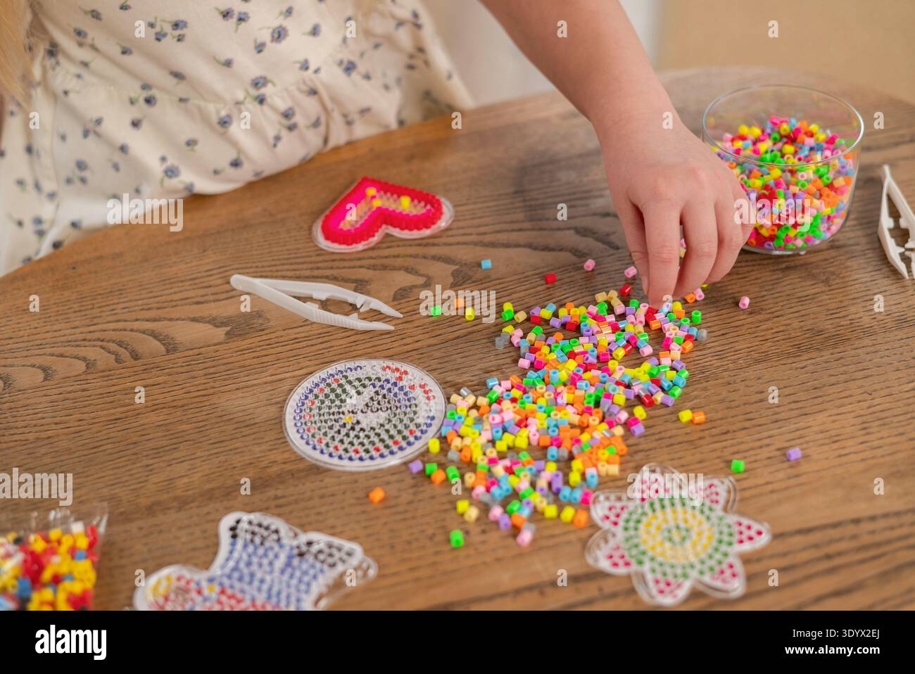 Kind spielt mit bunten Sicherungsperlen und Stiften an einem Holztisch. Thermomosaische Perlen Stockfoto