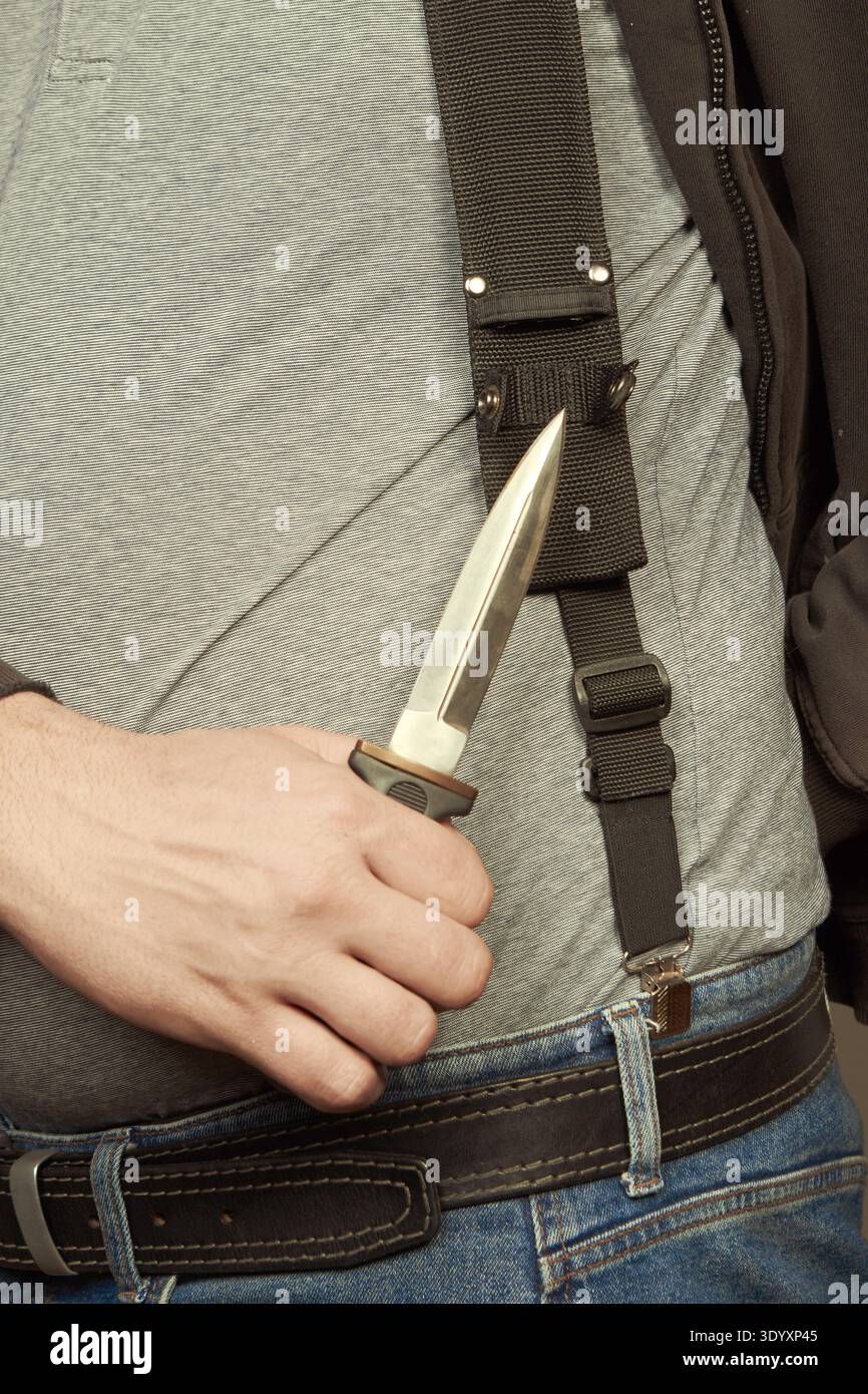 Mann in schwarzem Kapuzenhemd und schwarzem Hut, der seinen Dolch zeigt Stockfoto