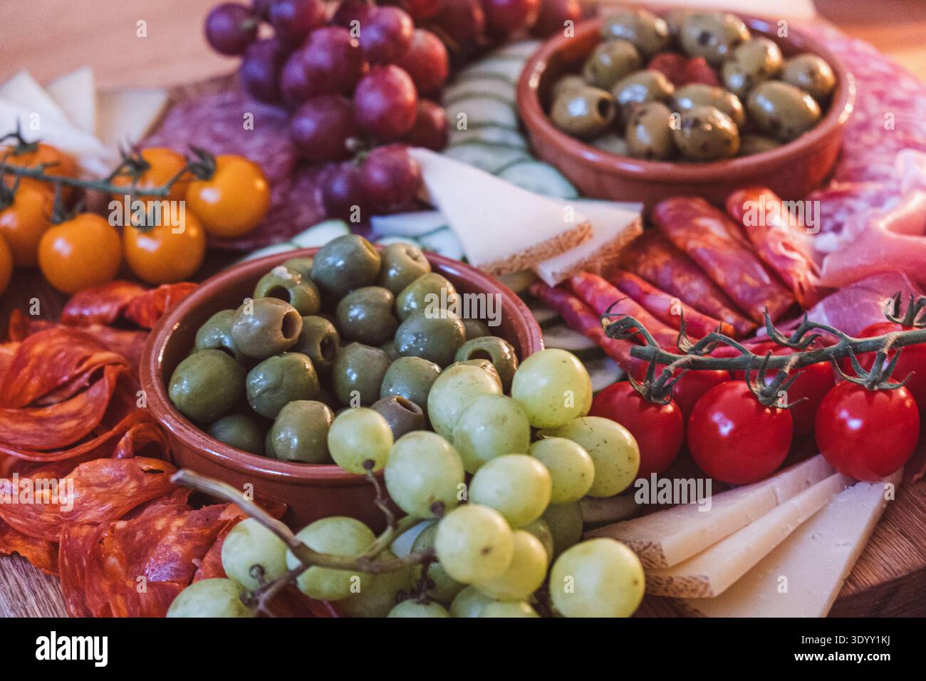 Wurstplatte mit Oliven, Trauben, Wurstwaren und Käse auf rustikalem Holztisch für Tapas im mediterranen Stil Stockfoto