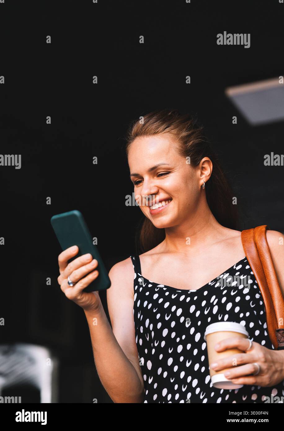 Frau in der Stadt mit Kaffee zum Mitnehmen unterwegs mit ihrem Smartphone. Stockfoto