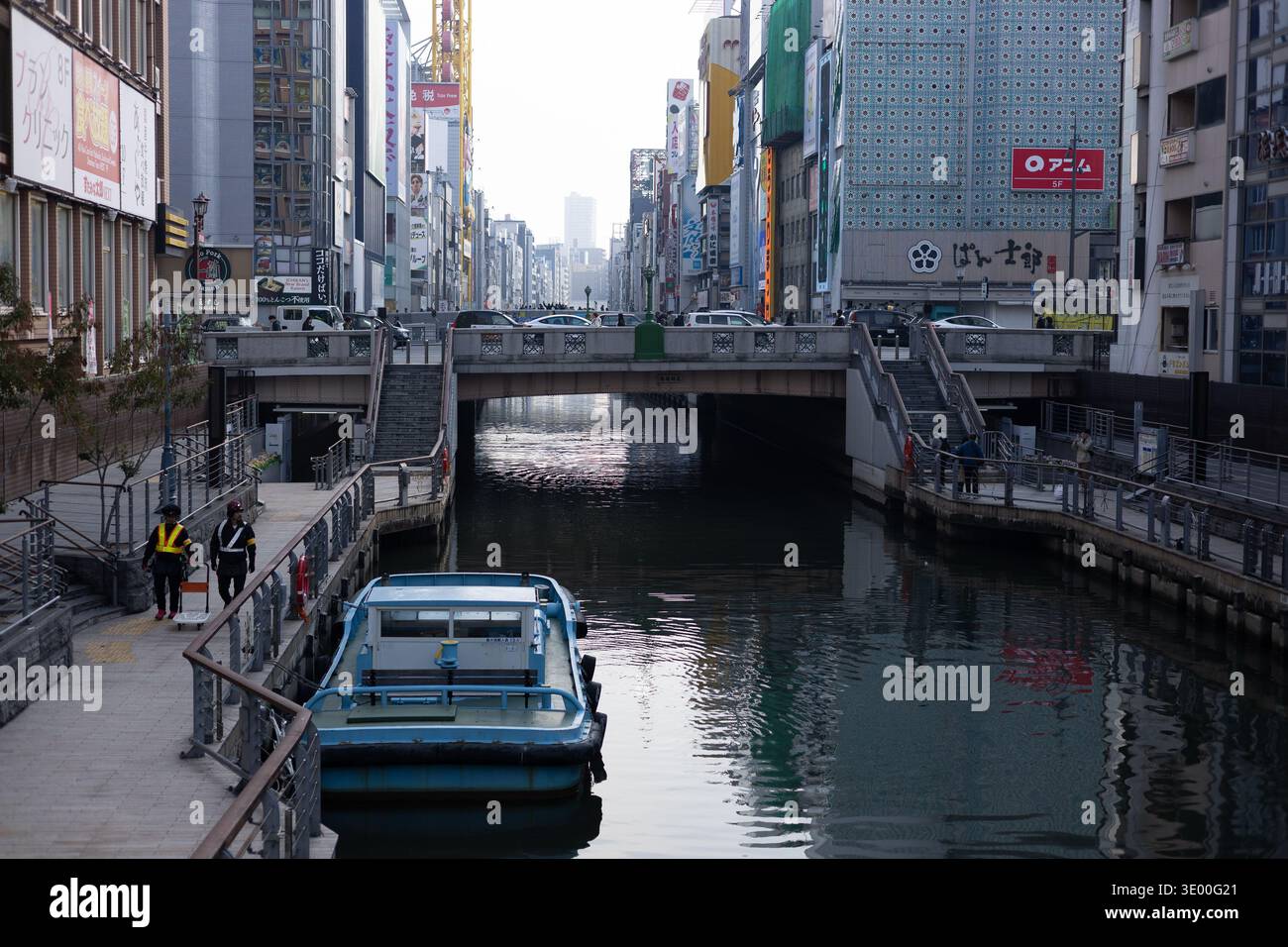 Kanalboot auf dem Dotonbori Wasserweg mit Arbeitern und farbenfrohen Geschäftsgebäuden entlang des Kanals, Osaka, Japan. Nur redaktionelle Verwendung. Stockfoto