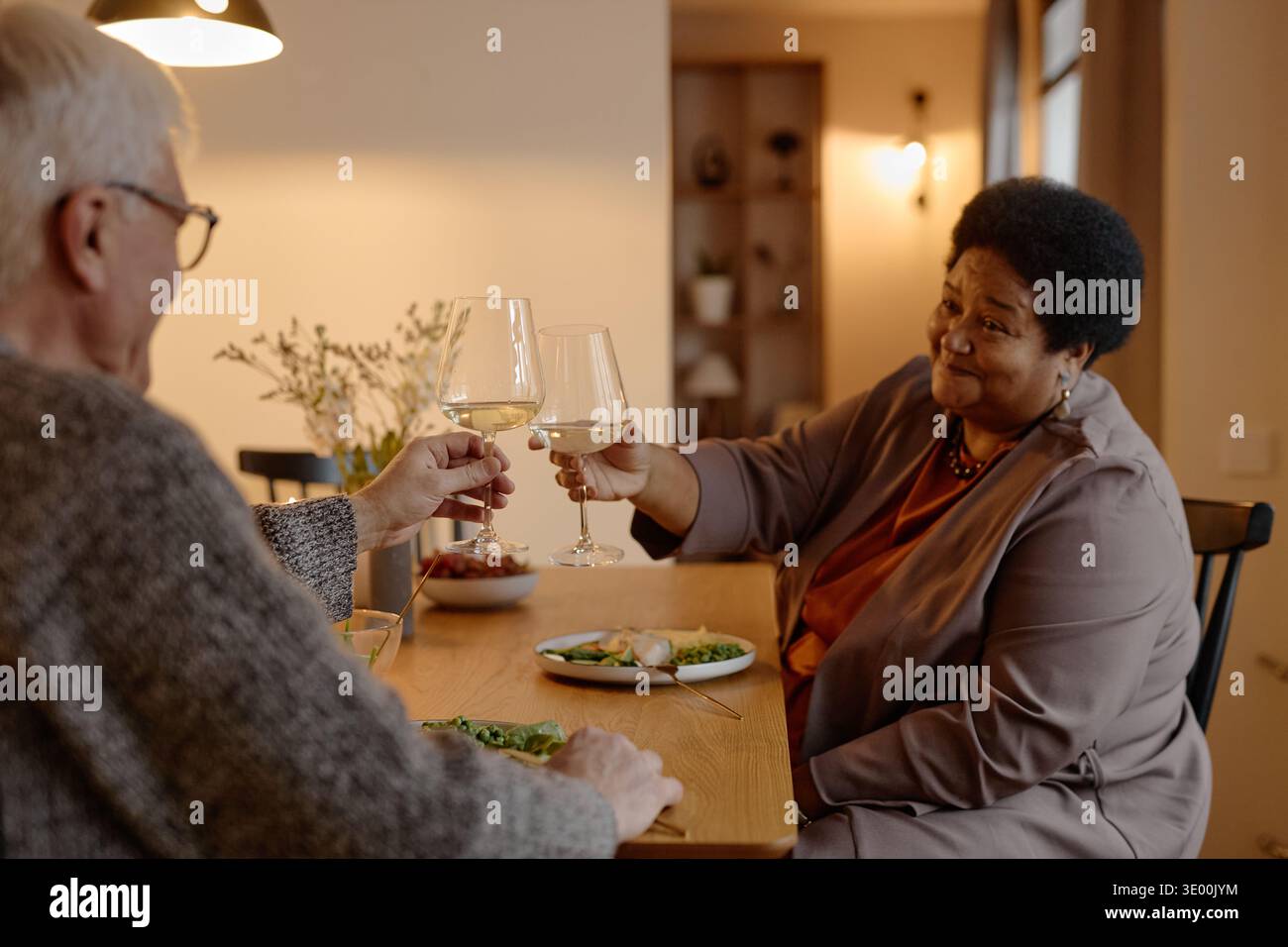Senior-kaukasischer Mann und Schwarze Frau, die Weingläser am Esstisch toasten Stockfoto